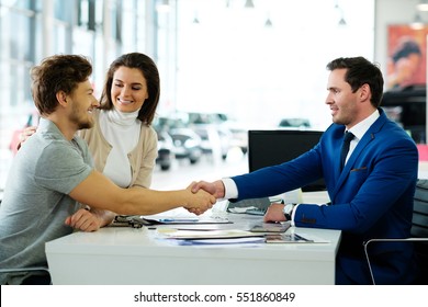 Salesman and customer shaking hands congratulating each other at the dealership showroom.