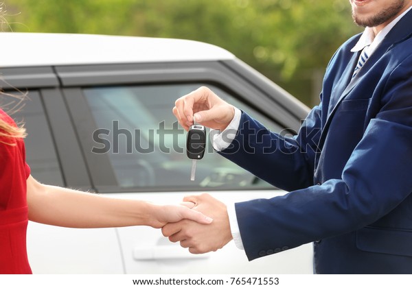 Salesman giving car\
key to customer\
outdoors