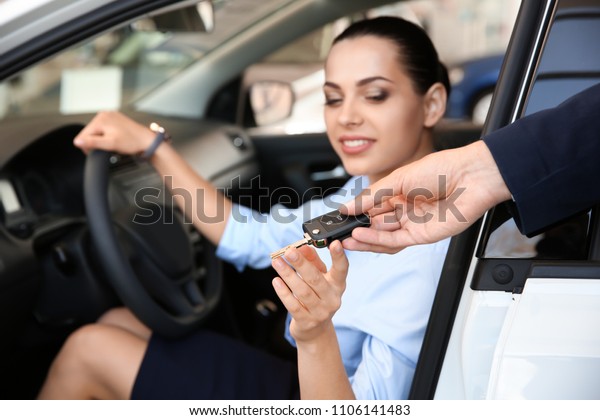 Salesman giving car key to woman on driver\'s\
seat of automobile