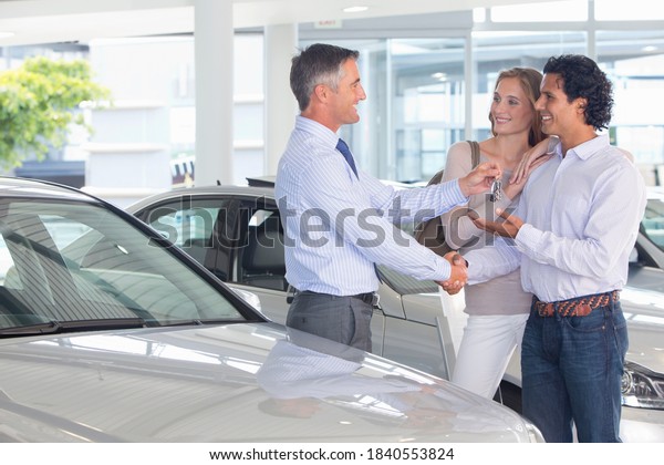 Salesman giving couple car keys in a car\
dealership showroom
