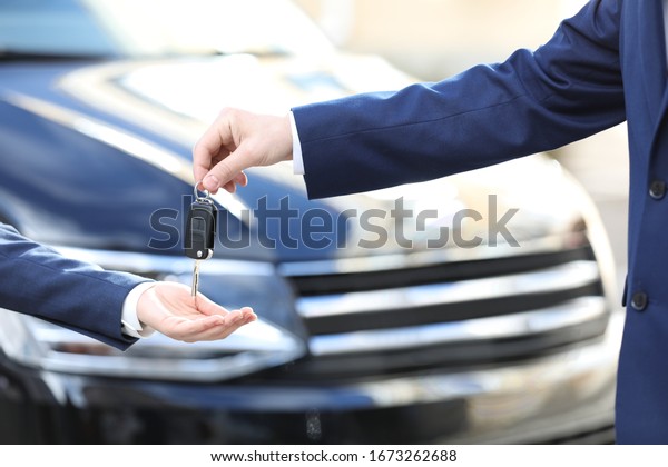 Salesman giving key to customer in modern auto\
dealership, closeup. Buying new\
car