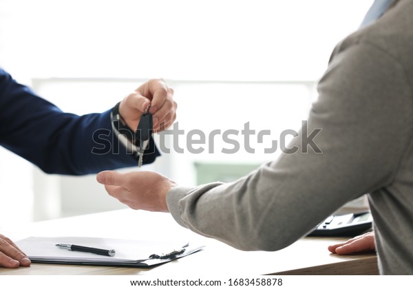 Salesman giving key to customer in office, closeup.\
Buying new car