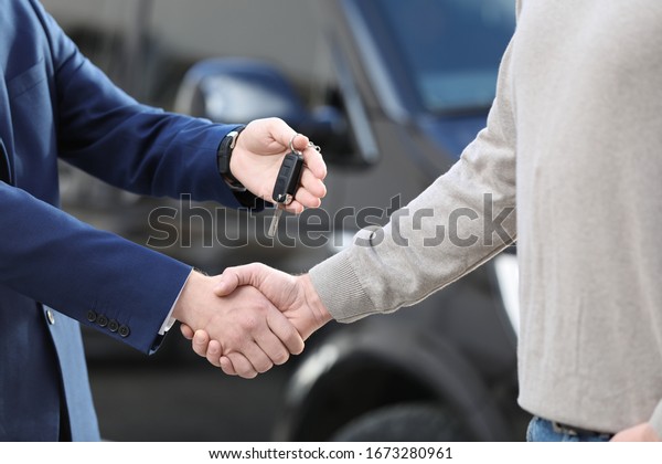 Salesman giving key
to customer while shaking hands in modern auto dealership, closeup.
Buying new car