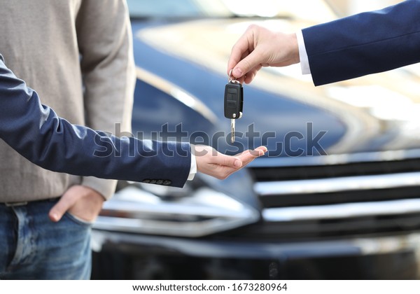 Salesman giving key to customers in modern auto\
dealership, closeup. Buying new\
car