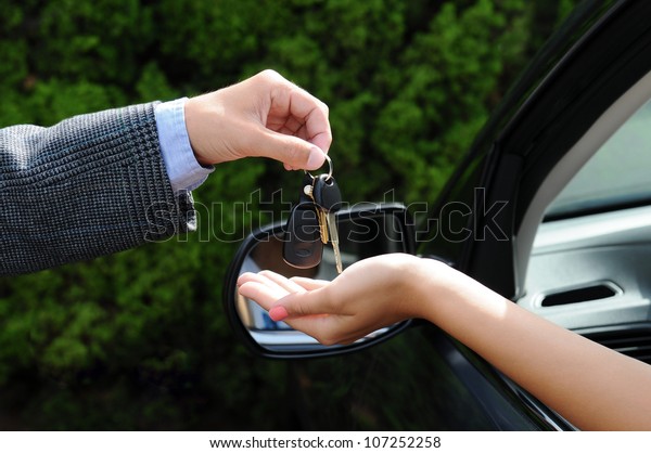 Salesman handing over the keys to a new car.\
Closeup of the man\'s hand handing keys to the woman\'s hand sticking\
out the window of the\
vehicle.