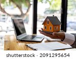 Salesman holding an orange model of a small house, a housing project salesman is drafting a sales contract for a customer who reserves a house in a project he maintains. Real estate trading concept.