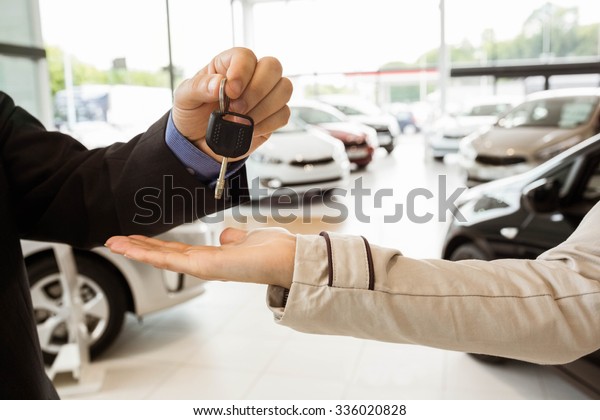 Salesman offering car key to a customers at new\
car showroom