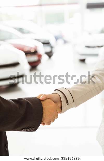 Salesman\
shaking a customer hand at new car\
showroom