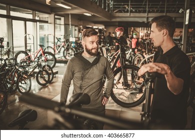 Salesman Showing A New Bicycle To Interested Customer In Bike Shop.