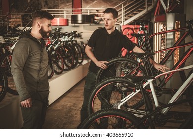 Salesman Showing A New Bicycle To Interested Customer In Bike Shop.