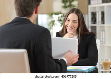 Salesman showing product from a tablet to a happy client who is looking at device in an office indoor