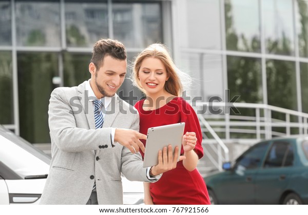 Salesman with tablet and client standing near\
new car outdoors