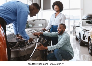 Salesman Talking To Young Black Couple, Showing Them New Luxury Car At Auto Dealership. African American Clients Buying Or Renting Automobile At Showroom. Vehicle Local Distribution Concept