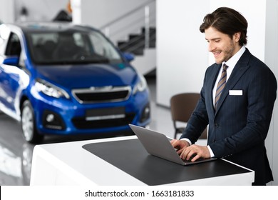 Salesman At Work. Car Dealer Standing At Desk In Luxury Dealership Office, Using Laptop, Empty Space