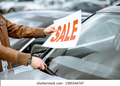 Salesperson putting sale plate on the car windshield on the open ground of a dealership, close-up view