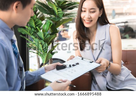 Salesperson workin at car dealership.Young Asian female consultant and couple buyers signing contract for new car in auto show. Concept for car rental or sale.