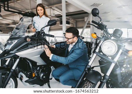 Saleswoman at the dealership showroom talking with customer and helping him to choose a new motorcycle for himself.