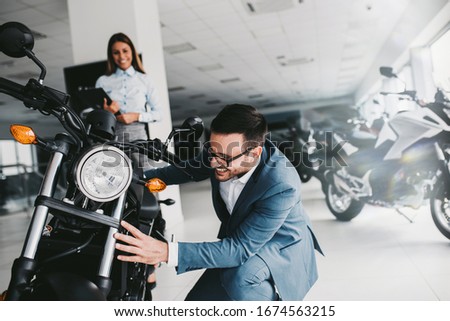 Saleswoman at the dealership showroom talking with customer and helping him to choose a new motorcycle for himself.