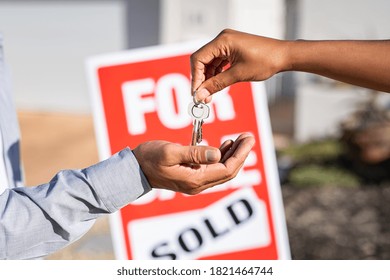 Saleswoman Giving Home Keys To New Property Owner. Close Up Of Real Estate Agent Hand Giving House Keys To Man. Agent Giving Apartment Key To New Owner After Putting The Word Sold On For Sale Sign.