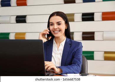 Saleswoman Talking On Phone At Desk In Car Dealership