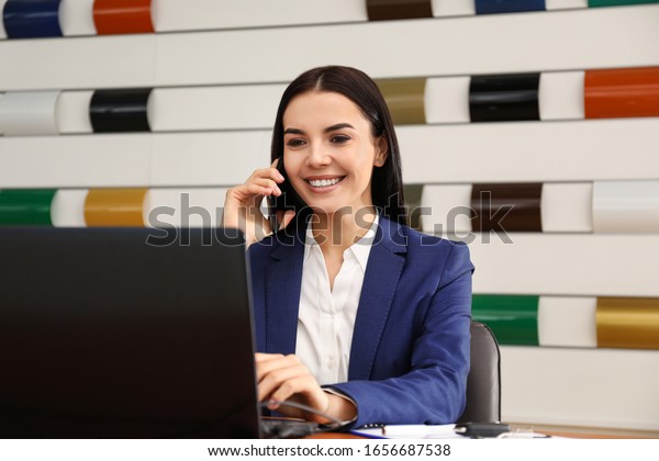 Saleswoman\
talking on phone at desk in car\
dealership