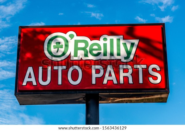 Salisbury, NC/USA - November 12, 2019: View looking\
up from below at red, white and green rectangular free standing\
O\'Reilly Auto Parts sign with brand and logo against a bright\
saturated blue sky.