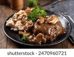 Salisbury steak with mushroom gravy garnished with parsley and mashed potatoes on a black plate