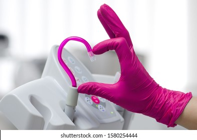 Saliva ejector and a hand in a disposable glove symbolize love in dentistry.Hand in a pink glove.Pink saliva ejector.The atmosphere of the dental office.With love in dentistry.Heart symbol.
