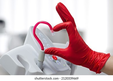 Saliva ejector and a hand in a disposable glove symbolize love in dentistry.Hand in a red glove.Red saliva ejector.The atmosphere of the dental office.With love in dentistry.Heart symbol.