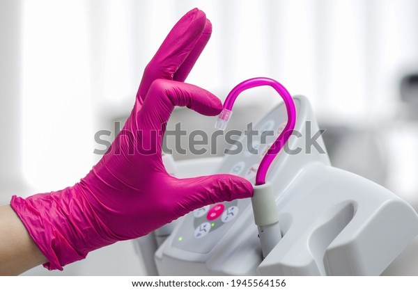 Saliva ejector and a hand in a disposable glove\
symbolize love in dentistry.Hand in a pink glove.Pink saliva\
ejector.The atmosphere of the dental office.With love in\
dentistry.Heart symbol.