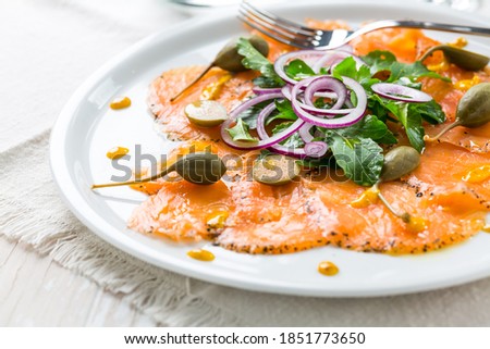 Salmon carpaccio and arugula salad with onions and capers on white plate