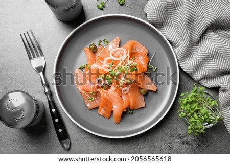 Salmon carpaccio with capers, onion and microgreens on grey table, flat lay