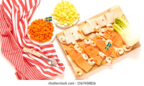 Salmon, Cod, Fennel On A Wooden Cutting Board. Potatoes And Carrots In White Plates. Spoon And Striped Tablecloth. Swedish Flags. Ingredients For Traditional Scandinavian Fish Soup. Swedish Food.