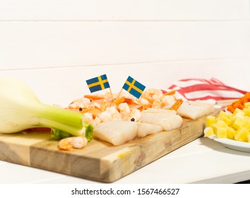 Salmon, Cod, Fennel On A Wooden Cutting Board. Potatoes And Carrots In White Plates. Spoon And Striped Tablecloth. Swedish Flags. Ingredients For Traditional Scandinavian Fish Soup. Swedish Food.