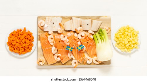 Salmon, Cod, Shrimps, Fennel On A Wooden Cutting Board. Potatoes And Carrots In White Plates. Swedish Flags. Ingredients For Traditional Scandinavian Fish Soup. Swedish Food.