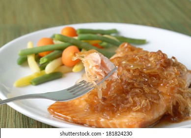 A Salmon Filet Baked In A Sweet Sauce Glaze And Topped With Caramelized Onions; Accompanied With Yellow And Green Beans, And Rounded Carrot Pieces.  