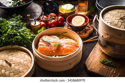 Salmon fillet in bamboo steamer on dark rustic kitchen table with ingredients. Healthy eating and cooking. Asian cuisine