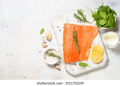 Salmon fillet with ingredients for cooking - sea salt, garlic and rosemary. Top view at white table with copy space.