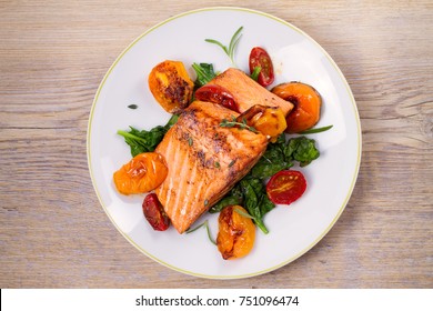 Salmon Fillet With Spinach And Tomatoes On White Plate On Rustic Wooden Background. Overhead, Top View