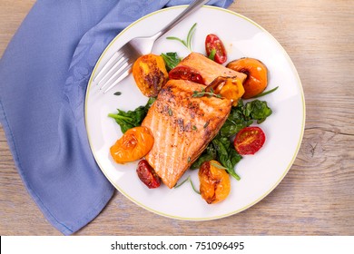 Salmon Fillet With Spinach And Tomatoes On White Plate On Rustic Wooden Background. Overhead, Top View