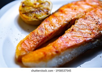 Salmon Fish Steak Cooked On Grill For Dinner.Delicious Red Fish Fillet Grilled In Sea Food Restaurant And Served On White Ceramic Plate With Lemons.Download Royalty Free Curated Food Images Collection