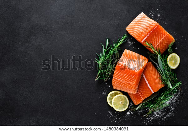 Salmon. Fresh raw\
salmon fish fillet with cooking ingredients, herbs and lemon on\
black background, top\
view
