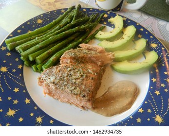 salmon with garlic sauce, asparagus and avocado on a white plate with a blue border and yellow stars