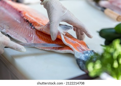 The salmon is in the hands of the experienced chef. She is using a knife to slice salmon fillet for sashimi and sushi. A chef cutting a salmon fillet with a knife on a cutting board. Cut fish fillet - Powered by Shutterstock