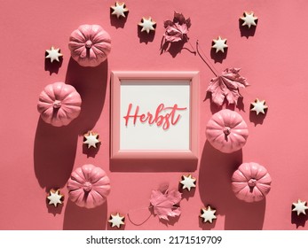 Salmon pink paper background with Autumn decor. Text Herbst in German language means Autumn. Monochromatic flat lay with star ginger cookies and maple leaves.