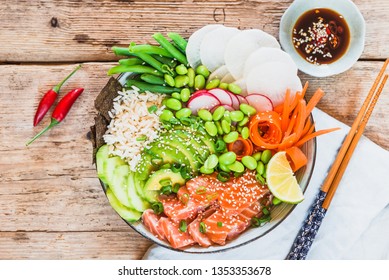 Salmon Poke Bowl With Avocado, Rice, Edamame Beans On Wooden Background Top View Copy Space.Trendy Healthy Asian Food.