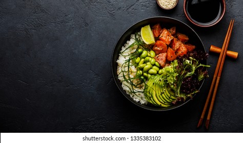 Salmon Poke Bowl Raw Fish Salad Asian Trendy Food With Soy Beans Edamame, Rice, Avocado And Lettuce In Bowl On Dark Background Copy Space