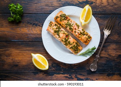 Salmon Roasted In An Oven With A Butter, Parsley And Garlic. Portion Of Cooked Fish And Fresh Lemon On A White Plate On The Wooden Background, Top View.