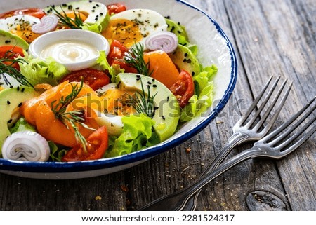 Salmon salad - smoked salmon, hard boiled eggs, avocado and leafy greens on wooden table 