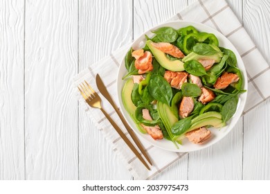 salmon spinach avocado and green pepper salad on a white plate with golden fork and knife on a white wood table, mediterranean healthy diet, horizontal view from above, flat lay, free space